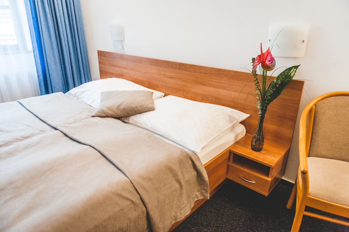 A neatly made bed with a wooden headboard, a bedside table with a vase of flowers, and a chair.