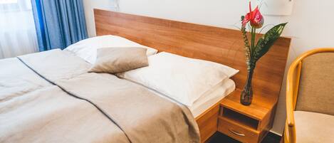 A neatly made bed with a wooden headboard, a bedside table with a vase of flowers, and a chair.