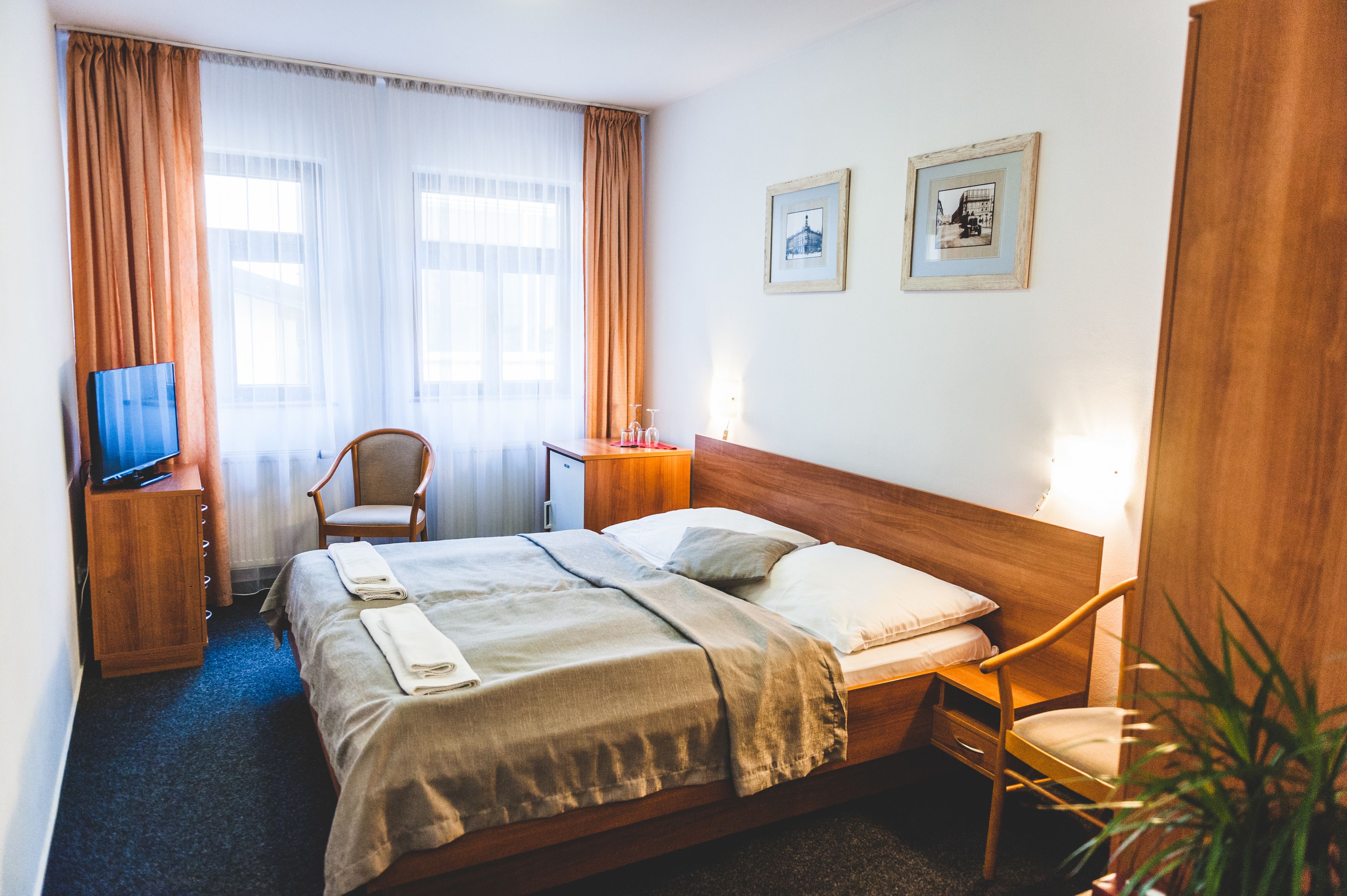 Une chambre d’hôtel avec un lit, une chaise, un bureau, un téléviseur et deux tableaux encadrés au mur.