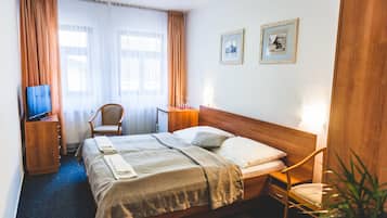Une chambre d’hôtel avec un lit, une chaise, un bureau, un téléviseur et deux tableaux encadrés au mur.