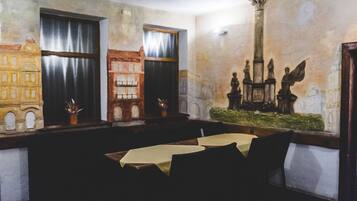 A dining area with a long table, chairs, and a mural on the wall depicting a historical scene.