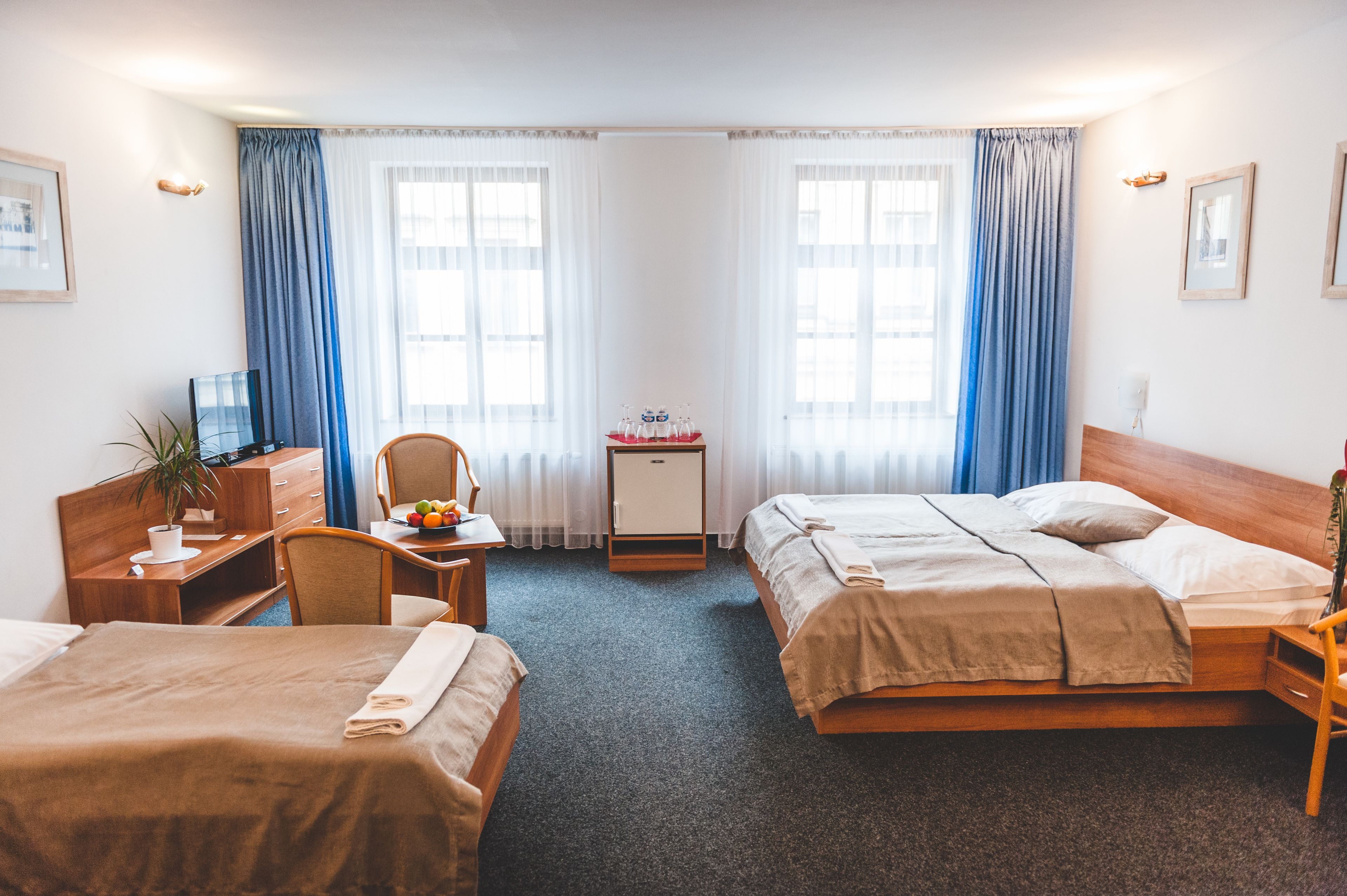 Une chambre d’hôtel avec deux lits, un bureau avec une chaise, un petit meuble et une plante en pot.