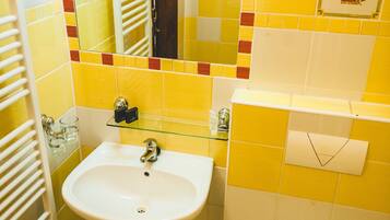 Een badkamer met gele en witte tegels, een wit wastafel, een spiegel, een toilet en een afvalbak.