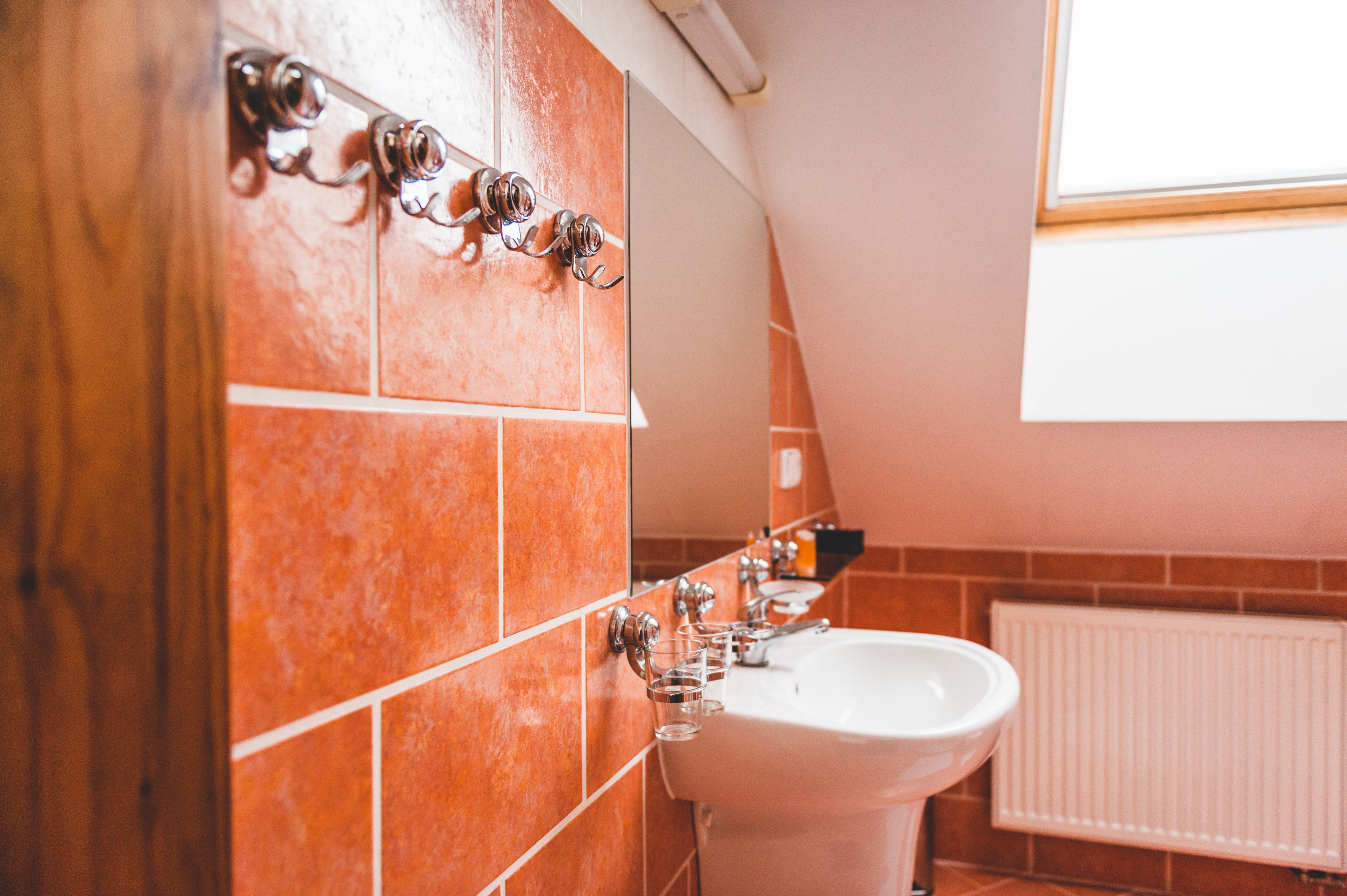 Un baño con azulejos anaranjados, un lavabo blanco y una ventana sobre el espejo.