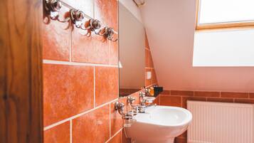 Un baño con azulejos anaranjados, un lavabo blanco y una ventana sobre el espejo.