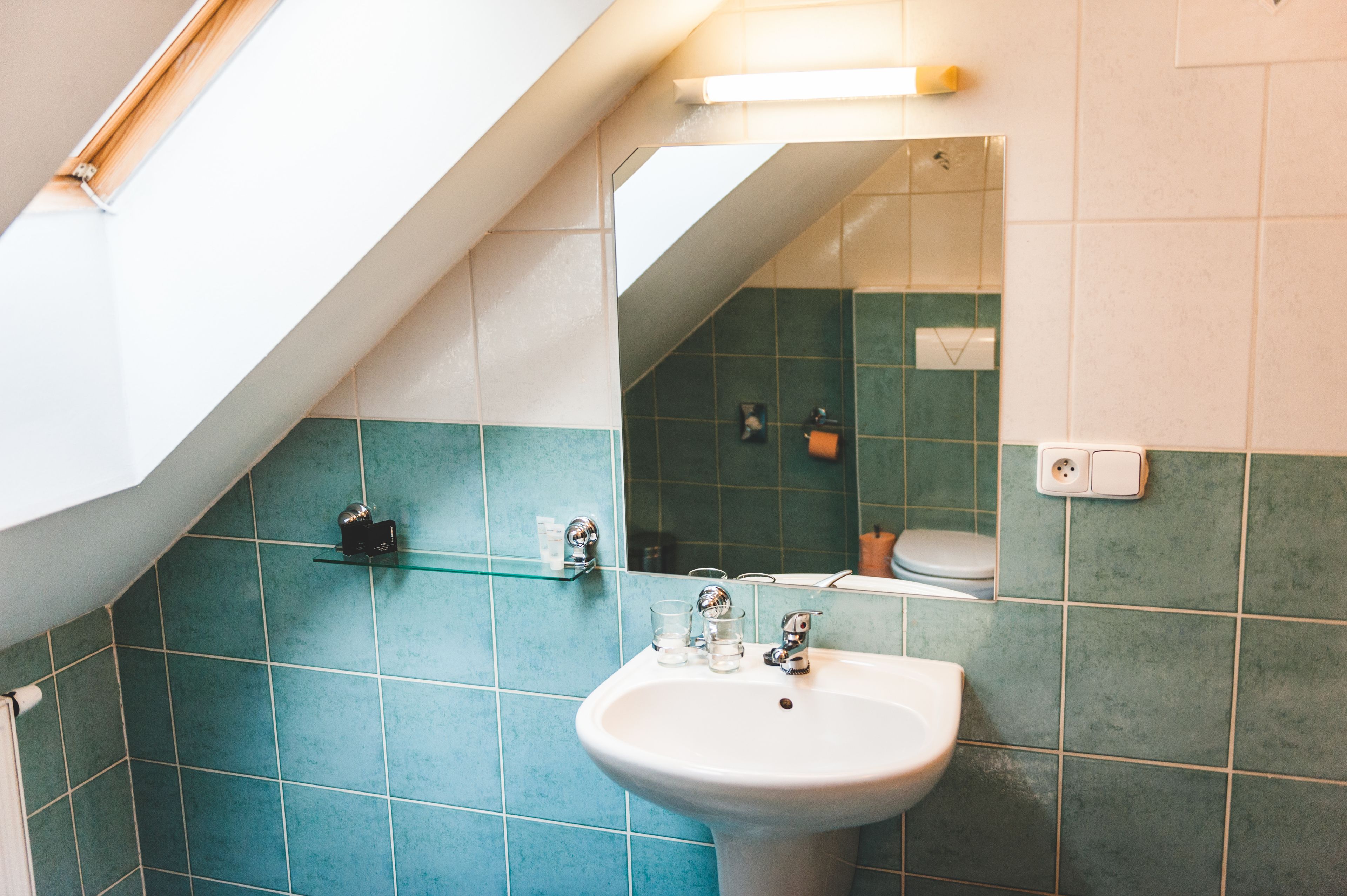 A bathroom with a white sink, green tiles, a mirror, and a skylight.