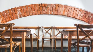 Een eetruimte met houten stoelen en tafels, een bakstenen boog en een betegelde vloer.