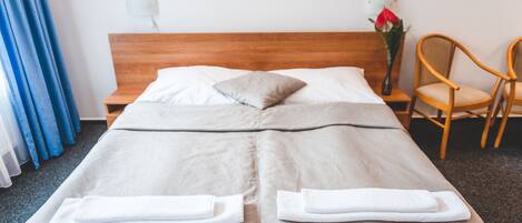 Een keurig opgemaakt bed met twee kussens, een houten hoofdbord, een nachtkastje met een bloemenvaas en een stoel.