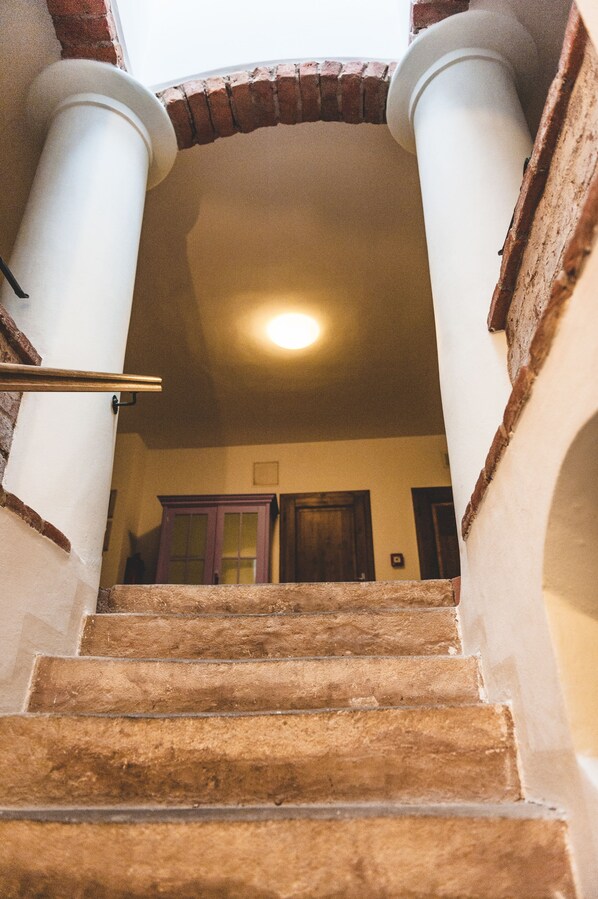 Un escalier orné de colonnes blanches et d’une arche en briques menant à une pièce dotée d’une porte et d’un luminaire.