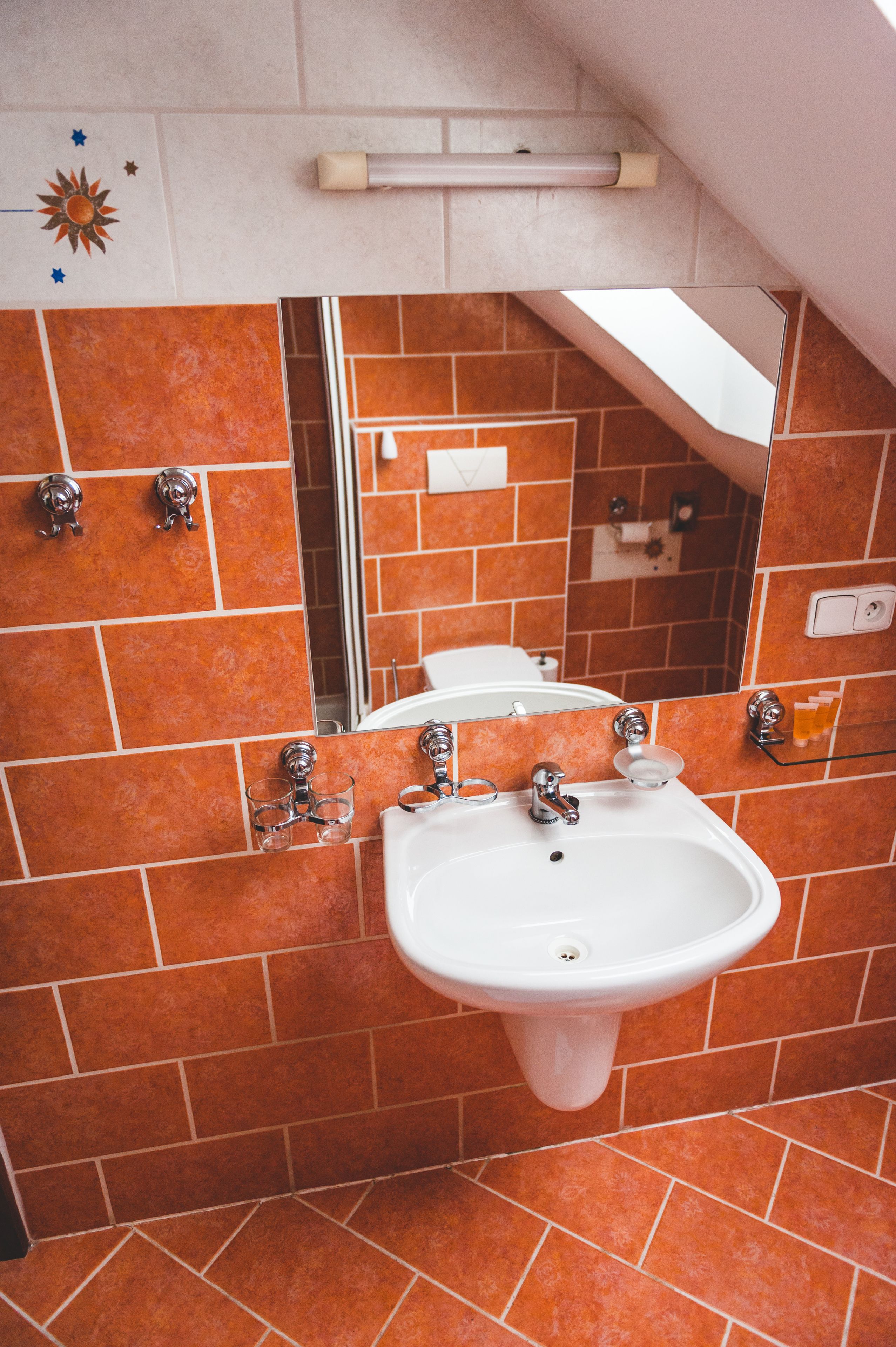 A bathroom with a white sink, orange tiles, a mirror, and a towel rack.