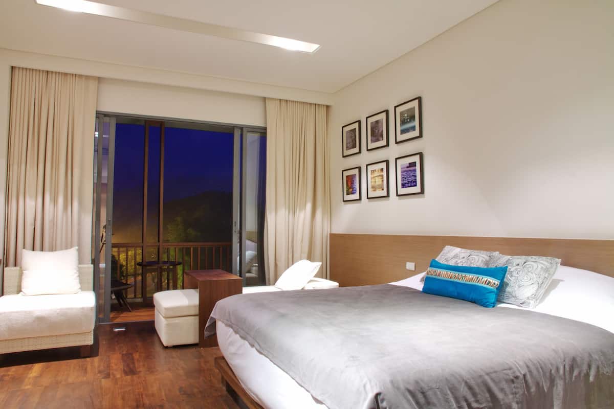 A hotel room with a large bed, a sofa, a small table, and a balcony with curtains.