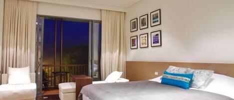 A hotel room with a large bed, a sofa, a small table, and a balcony with curtains.