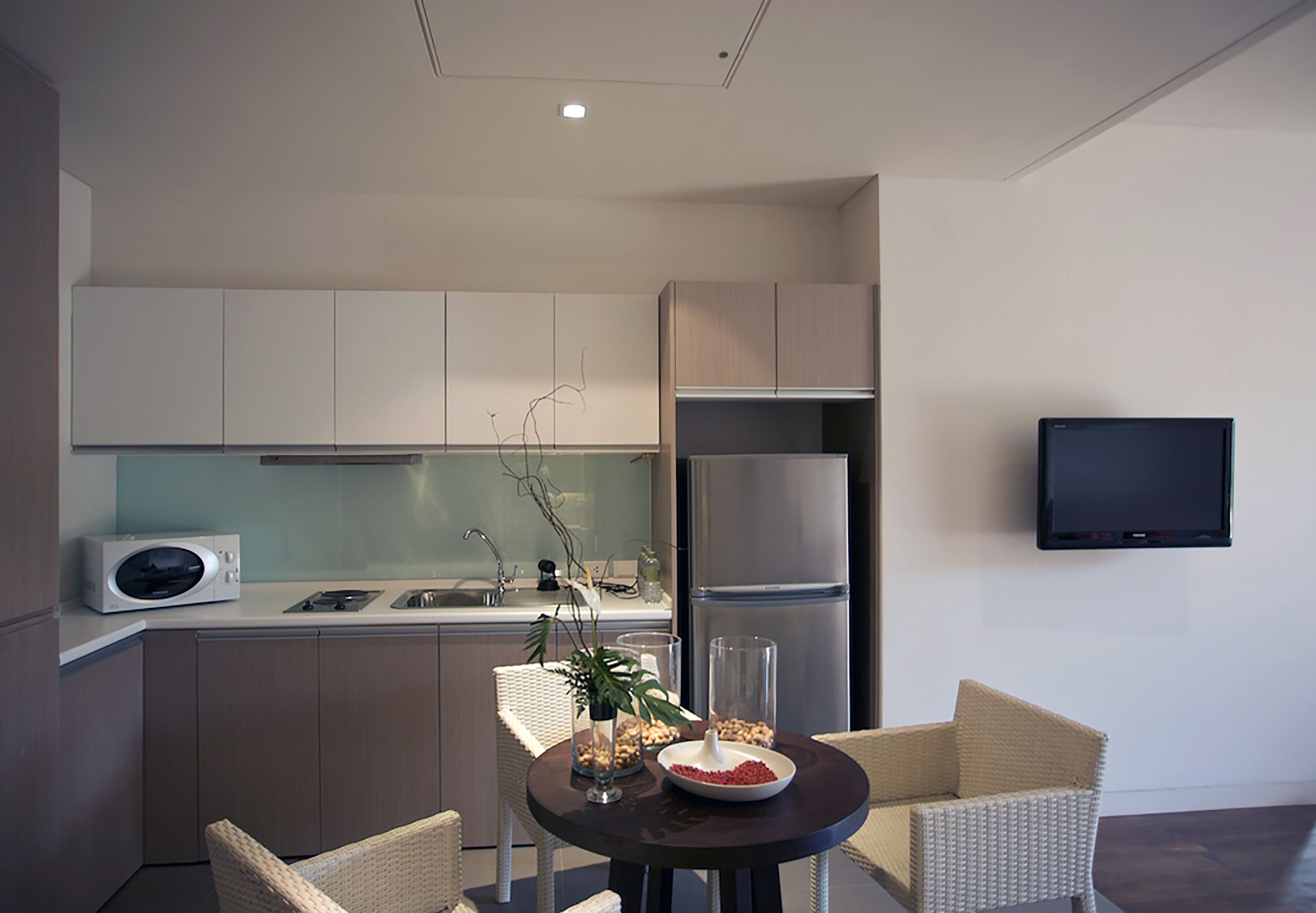 Une cuisine moderne avec des meubles blancs, un four à micro-ondes, un réfrigérateur et un coin repas agrémenté de chaises et d’une table en osier.