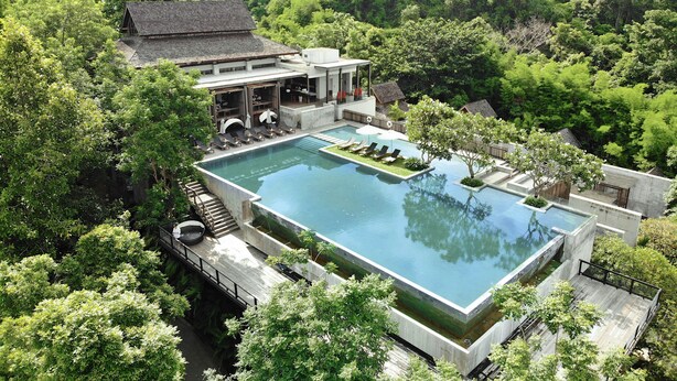 A modern resort with a large rectangular pool, lounge chairs, and a dining area surrounded by lush greenery. - Veranda Chiang Mai Suite (Hang Dong)