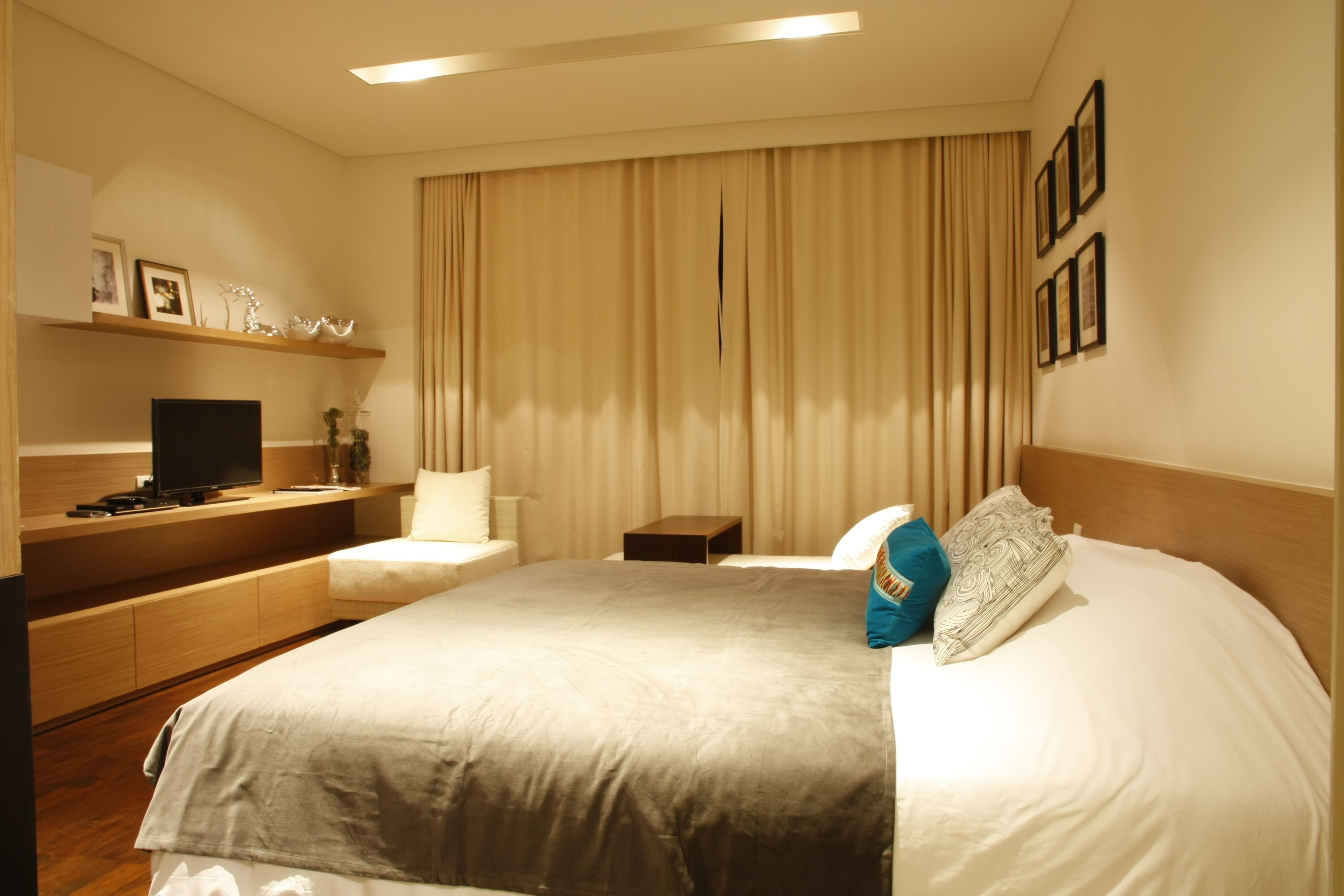 A hotel room with a large bed, a TV, a desk, and a shelf with decorative items.