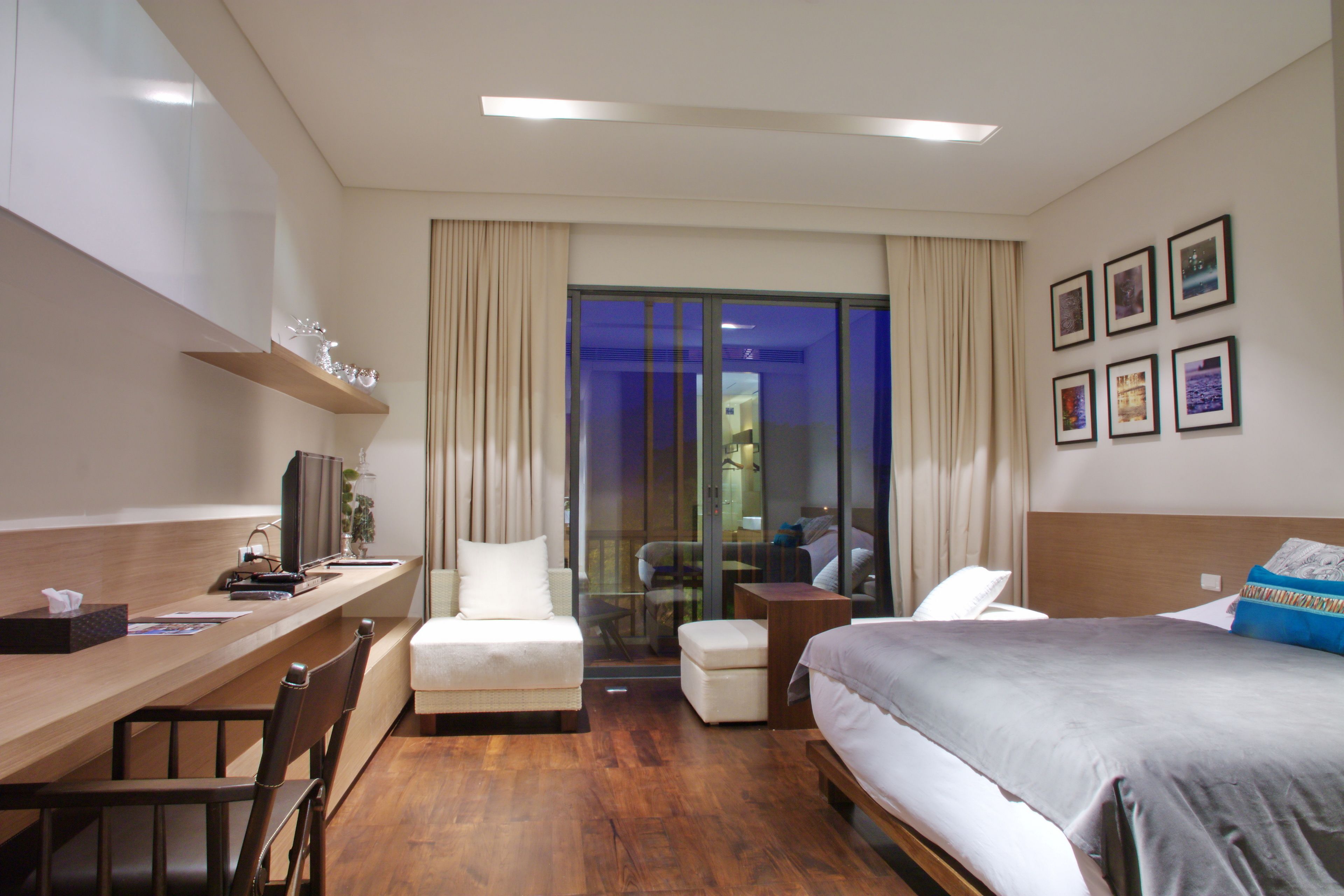 Habitación de hotel con un escritorio de madera, una cama, un sofá y un ventanal de vidrio que da a un balcón.
