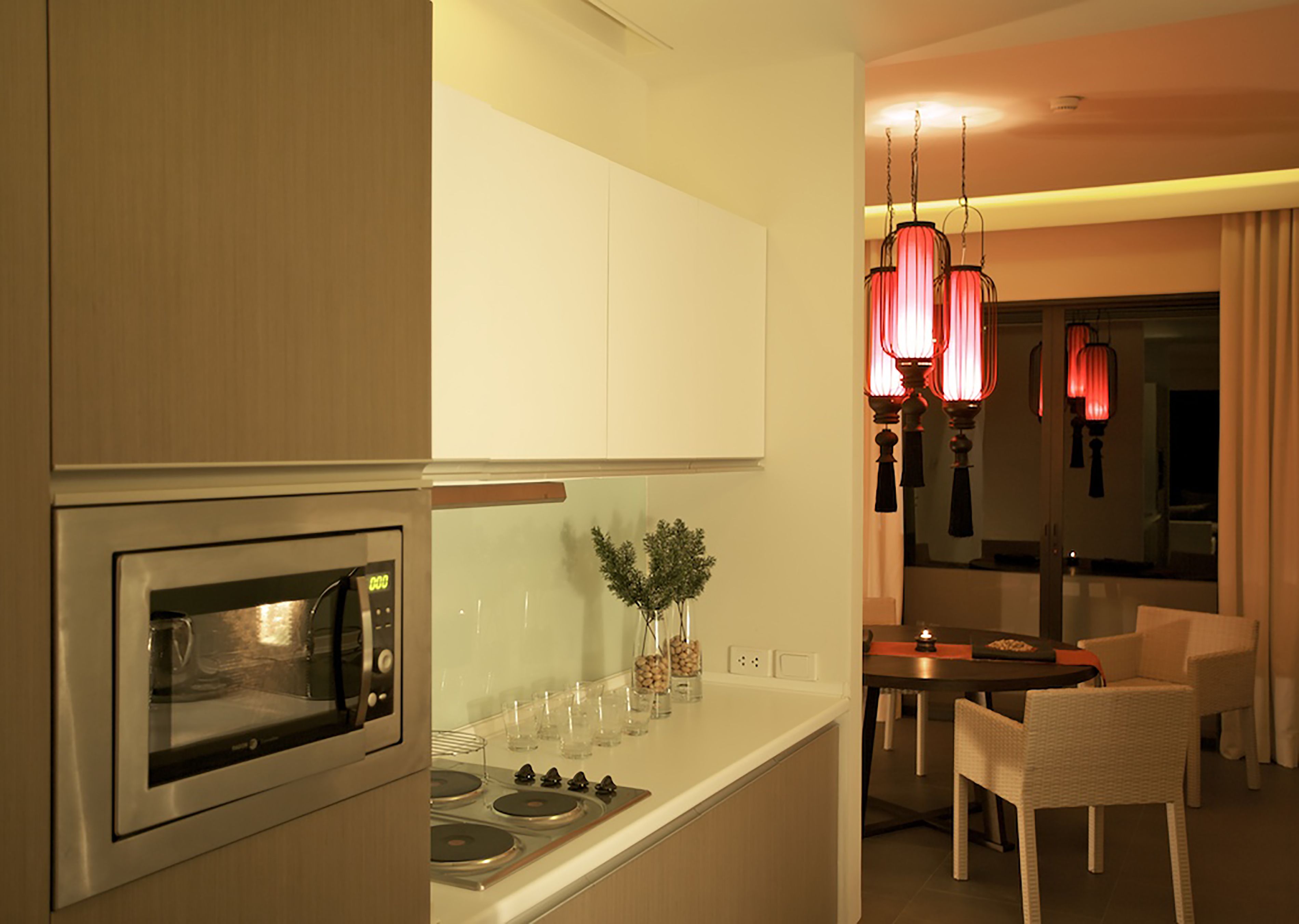 A modern kitchen with an integrated oven and stovetop, a dining area with a table and chairs, and a decorative red pendant light.