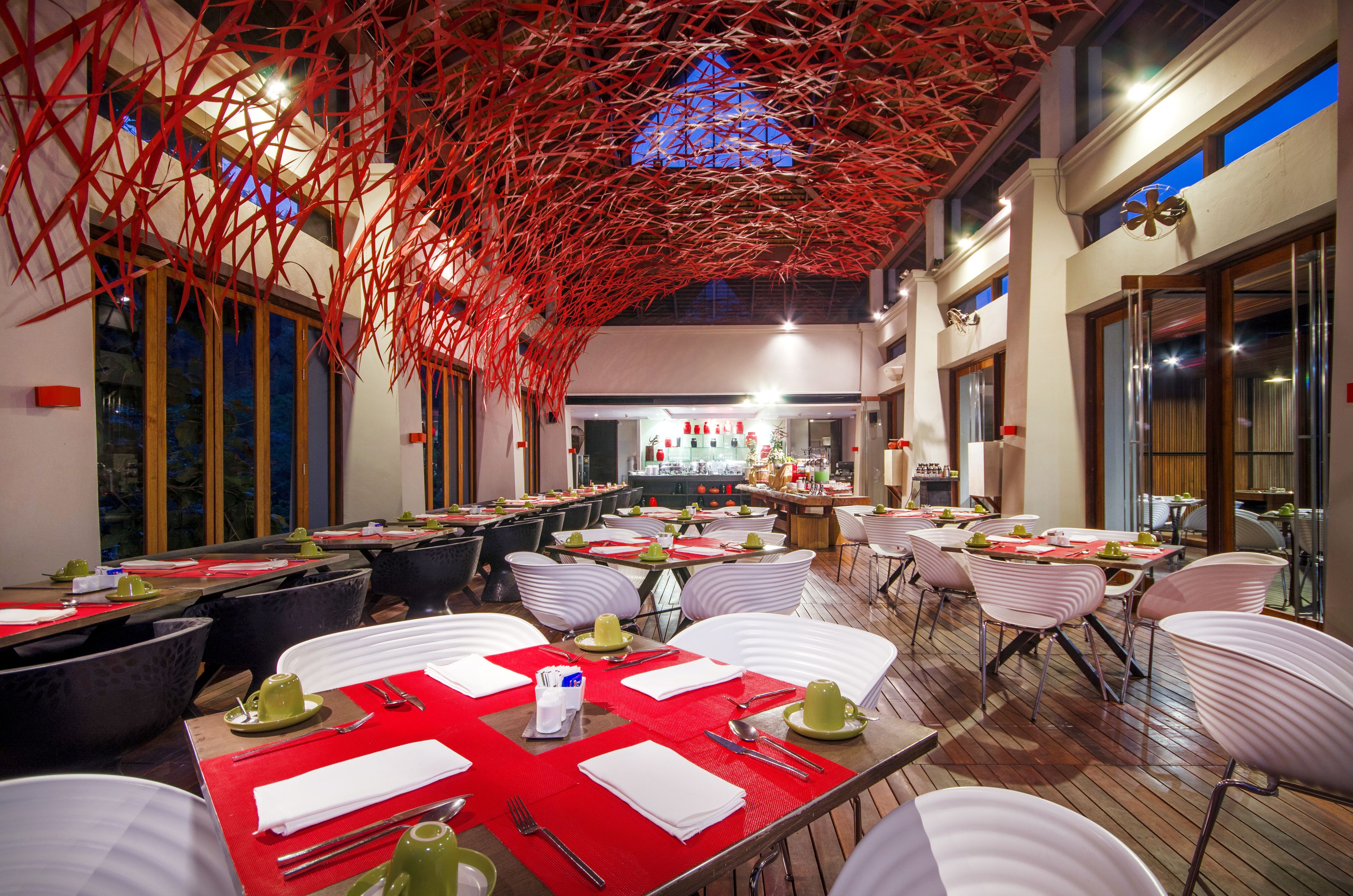 A restaurant with multiple tables set for dining, featuring red placemats and white chairs.