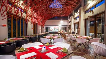 A restaurant with multiple tables set for dining, featuring red placemats and white chairs.