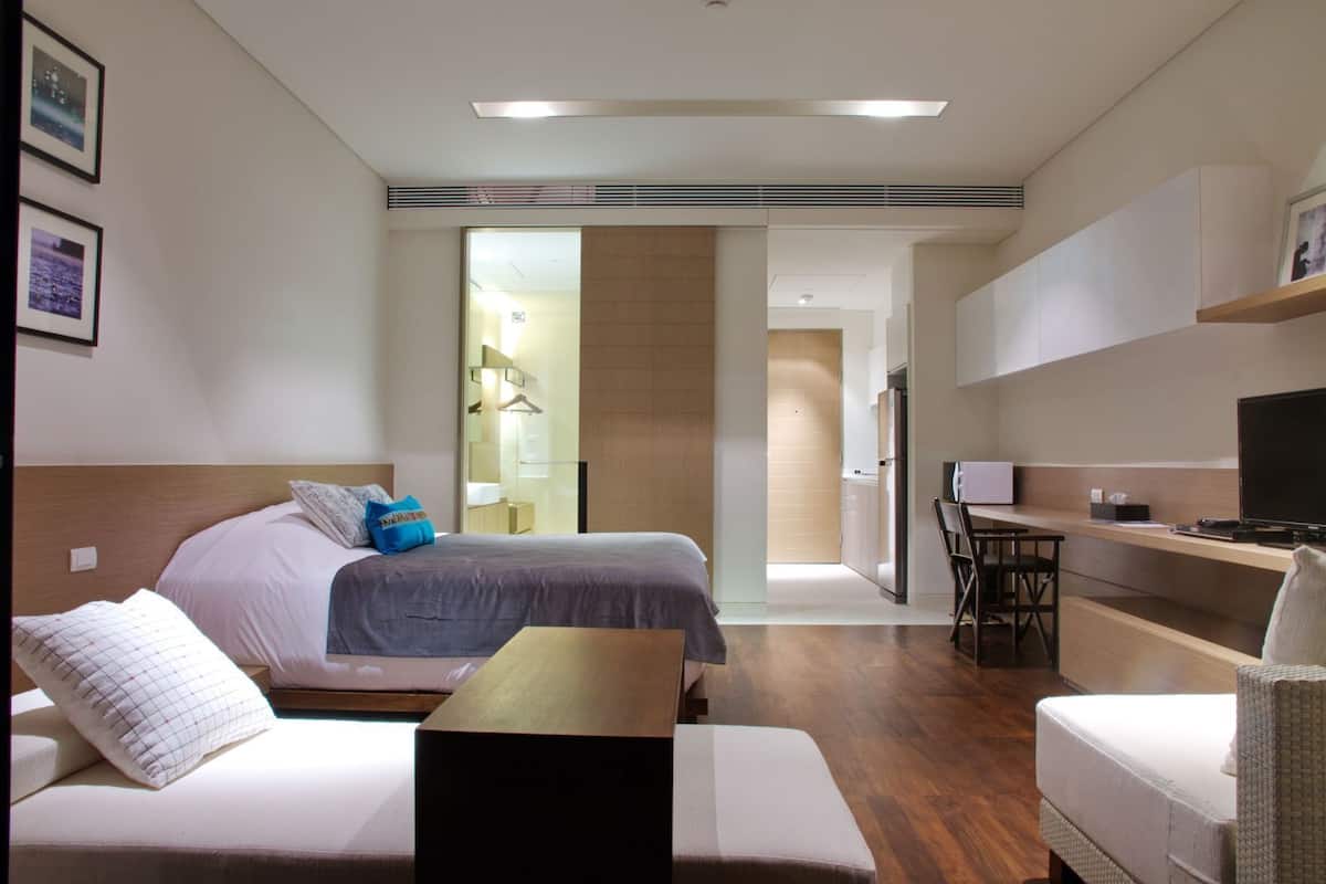 A hotel room with a bed, a sofa, a desk, a TV, and a bathroom visible through an open door.