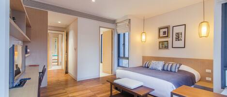 A modern hotel room with a large bed, a wooden bench, a desk, and a view of the hallway.