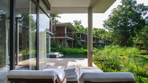 A modern outdoor lounge area with wooden loungers and a view of a pool and building complex. - Veranda Chiang Mai Suite (Hang Dong)