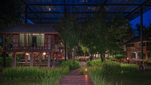 A wooden building with a covered outdoor area, a wooden pathway, and surrounding greenery. - Veranda Chiang Mai Suite (Hang Dong)
