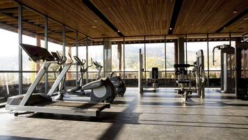 Ett gym med löpband, motionscyklar och styrketräningsmaskiner, stora fönster och ett träpanelat tak.