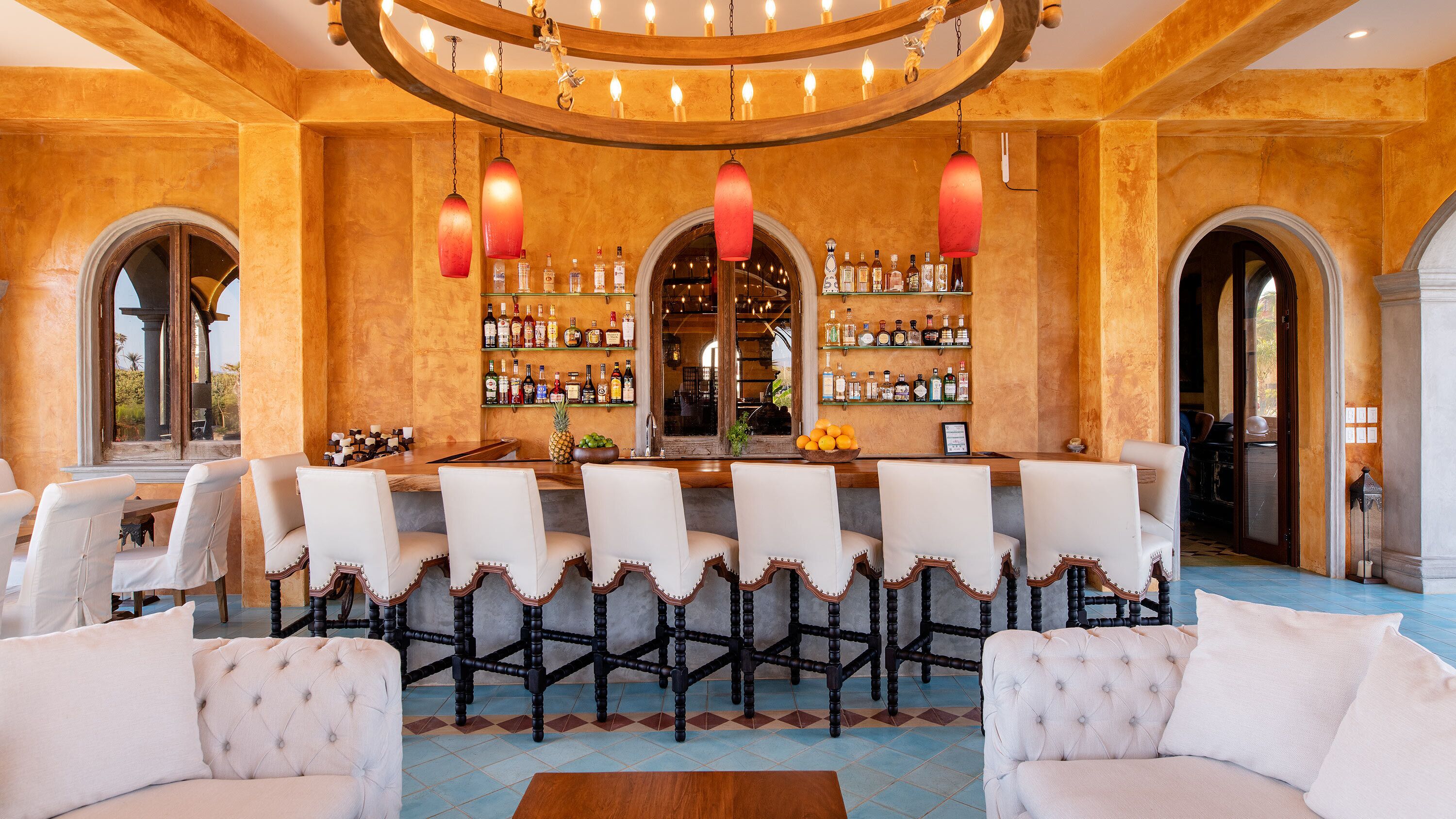 A bar area with a long counter, multiple chairs, and a variety of bottles.