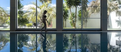 Una piscina techada, una piscina al aire libre, sombrillas