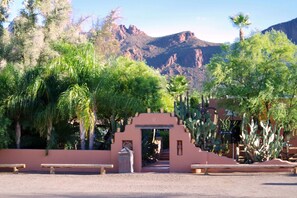 A desert landscape with a cactus garden, a wooden bench, and a pink archway leading to a building.