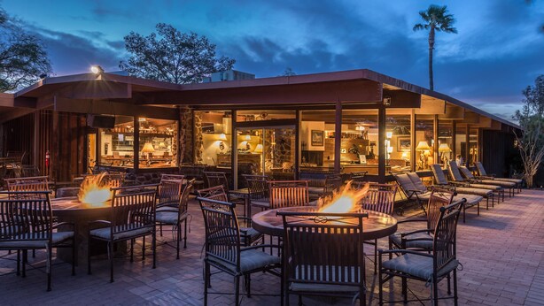 An outdoor seating area with fire pits and chairs, a covered bar area, and a view of the interior bar and dining space. - White Stallion Ranch (Tucson)