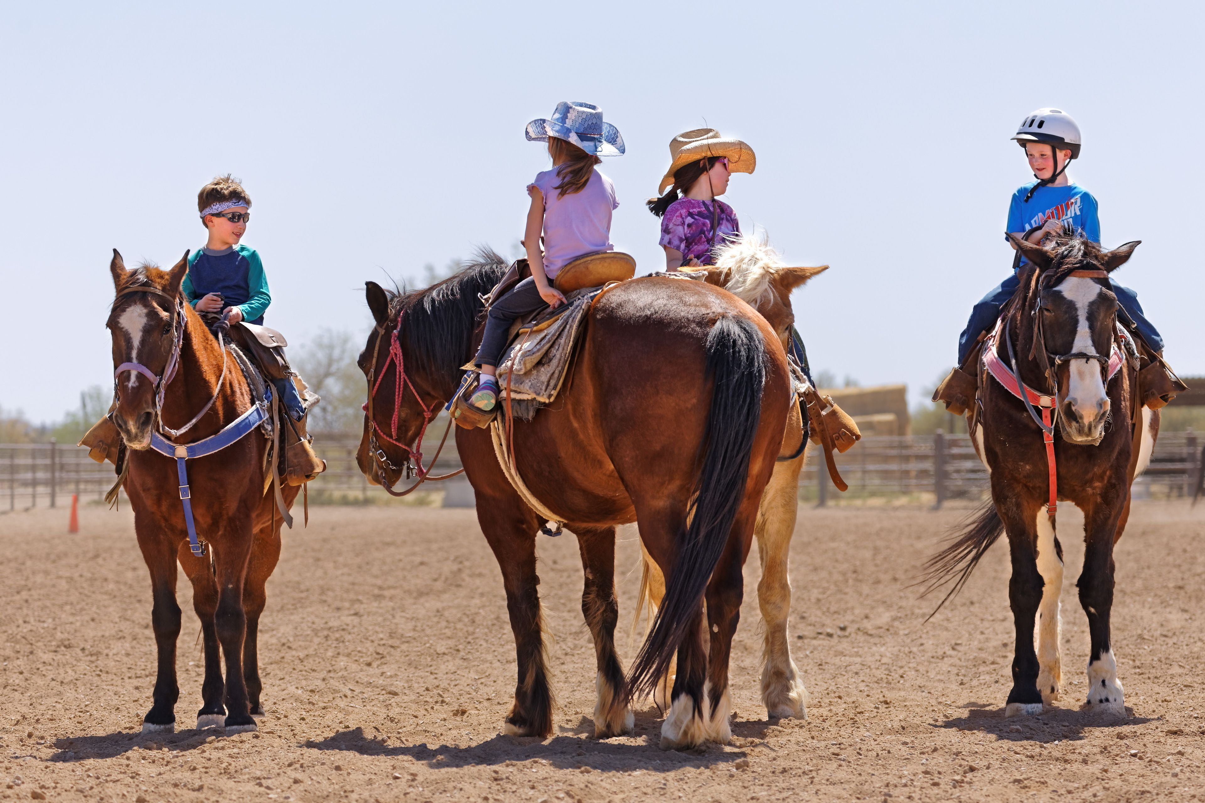 Three children riding horses in an outdoor arena.