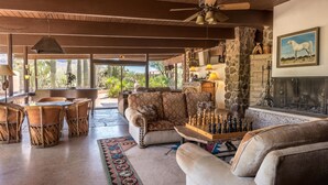 A spacious living area with a fireplace, a chessboard, and a large window overlooking a garden. - White Stallion Ranch (Tucson)