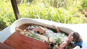 A person relaxing in a bathtub filled with water and citrus slices, surrounded by greenery. - Zen Resort Bali (Buleleng)
