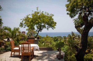 A patio with wooden furniture and a view of the ocean.