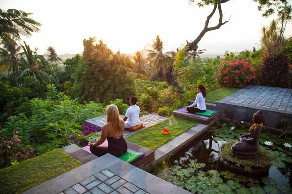 Un espacio sereno para meditación al aire libre con una estatua de Buda, abundante vegetación y una fuente de agua tranquila.