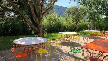 Un espace extérieur aménagé avec des tables et des chaises rondes, entouré d’arbres et de verdure.