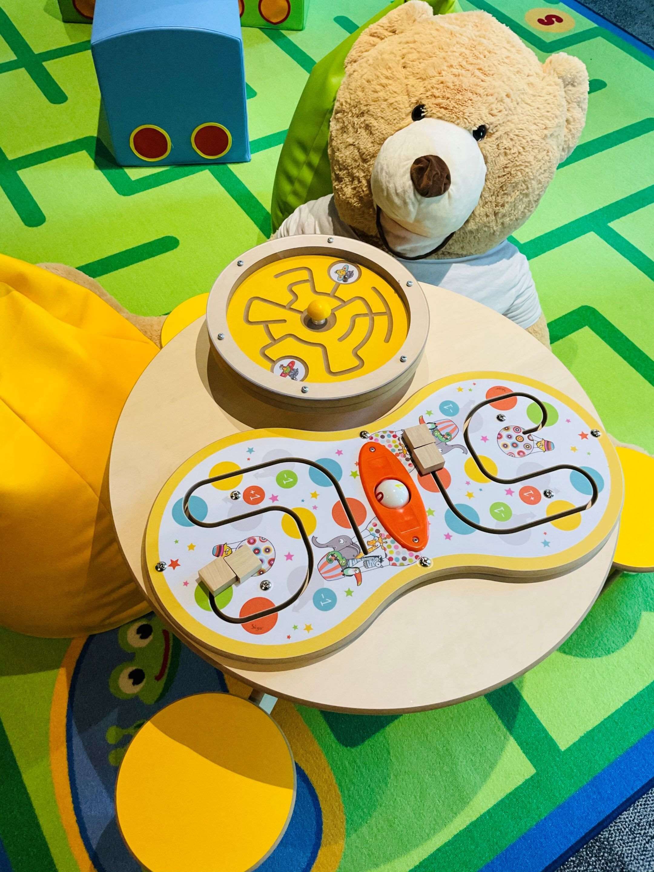 Un tapis de jeu avec un labyrinthe, une petite voiture et un ours en peluche.