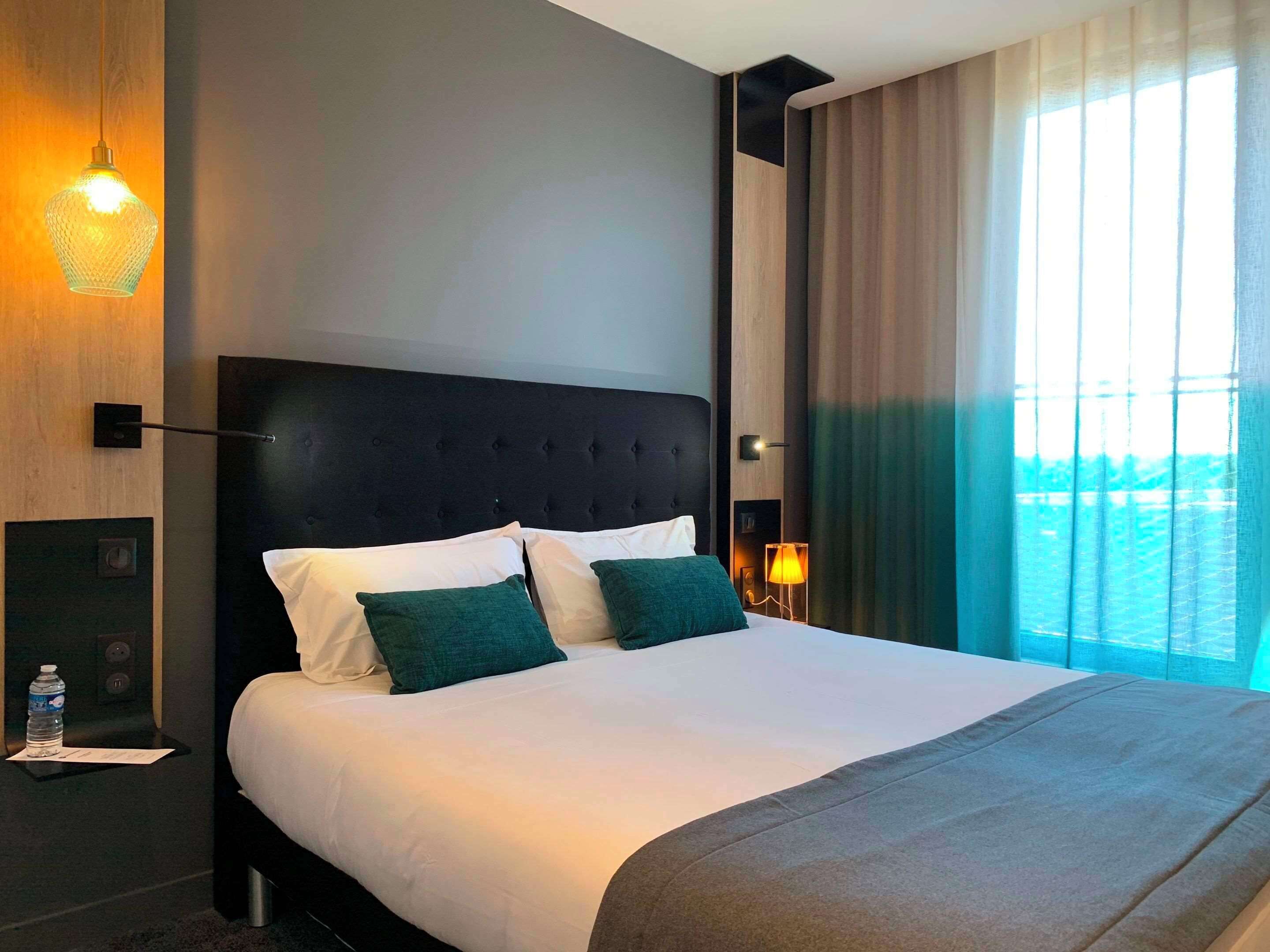 Una habitación de hotel moderna con una cama grande, cabecera oscura y vistas al mar a través de amplios ventanales.