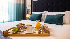 Un lit bien fait, avec un plateau contenant divers éléments pour le petit-déjeuner, notamment des fruits, du jus et du yaourt.