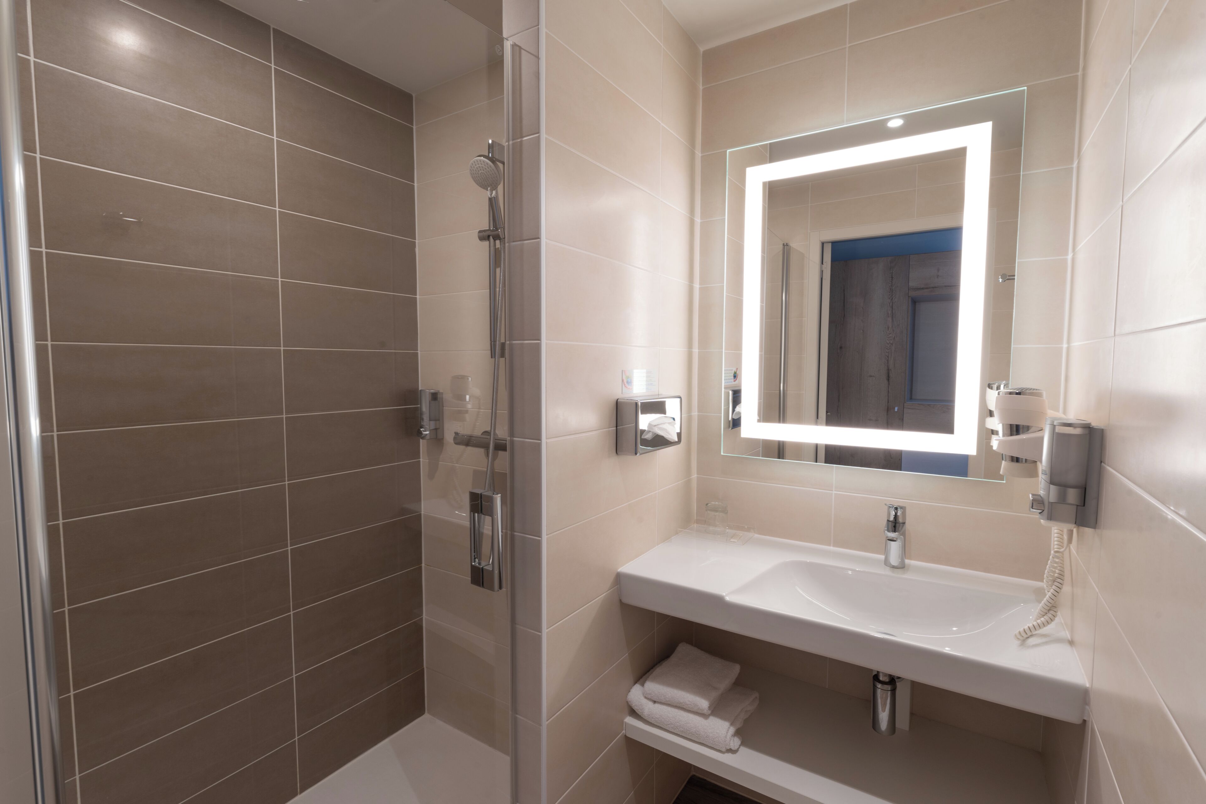 Un baño moderno con ducha de vidrio, un lavamanos blanco con espejo y un perchero para toallas.