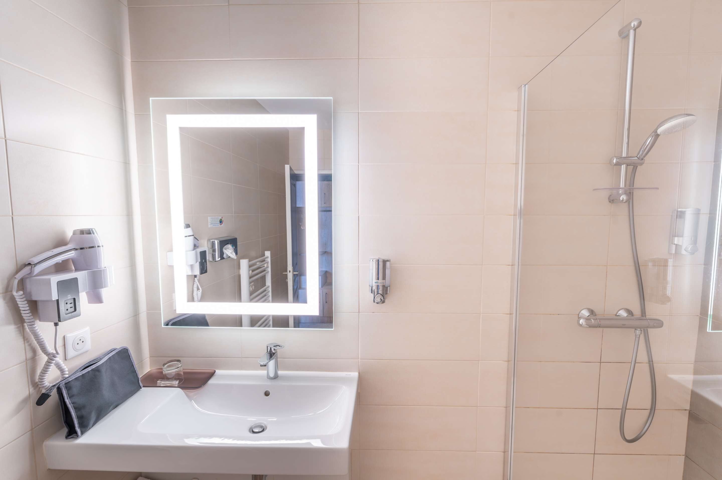 A bathroom with a white sink, a mirror, a handheld showerhead, and a hairdryer on a wall-mounted station.