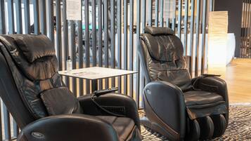Twee massagestoelen in een moderne ruimte met een gestreepte wand en een klein tafeltje.