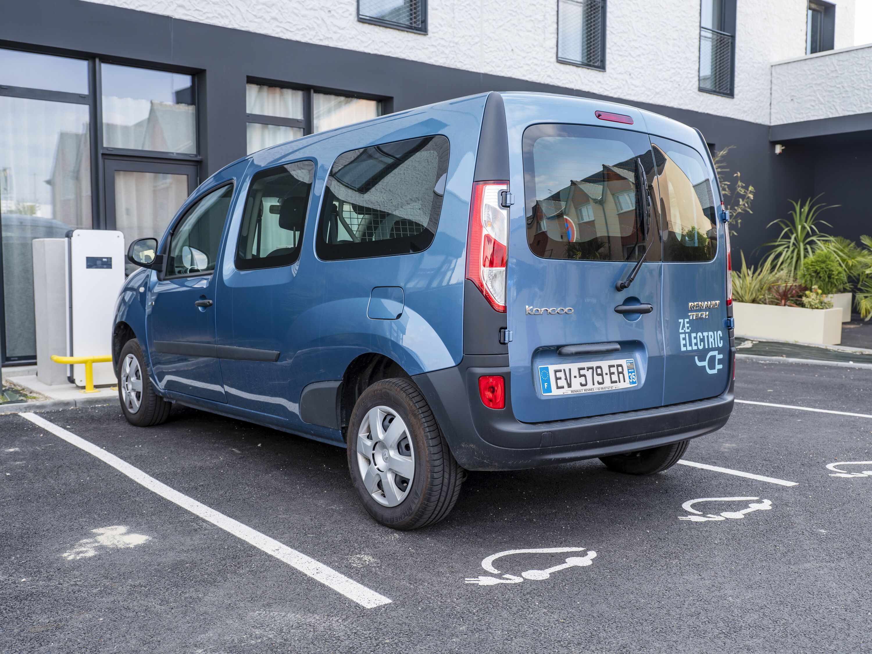 A blue electric vehicle parked in a designated parking space with a building in the background.