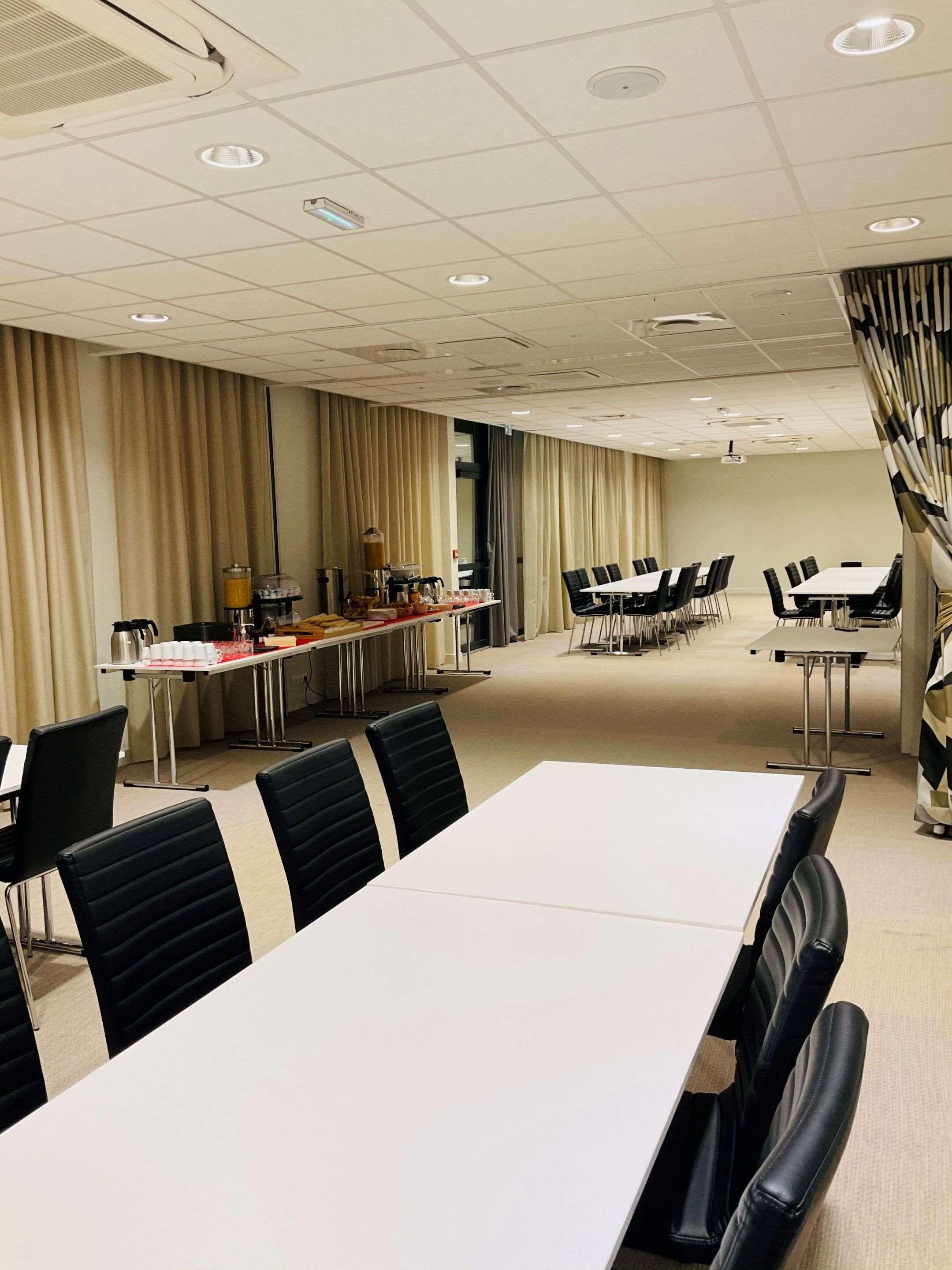 A conference room with a long table, black chairs, and a projector screen.