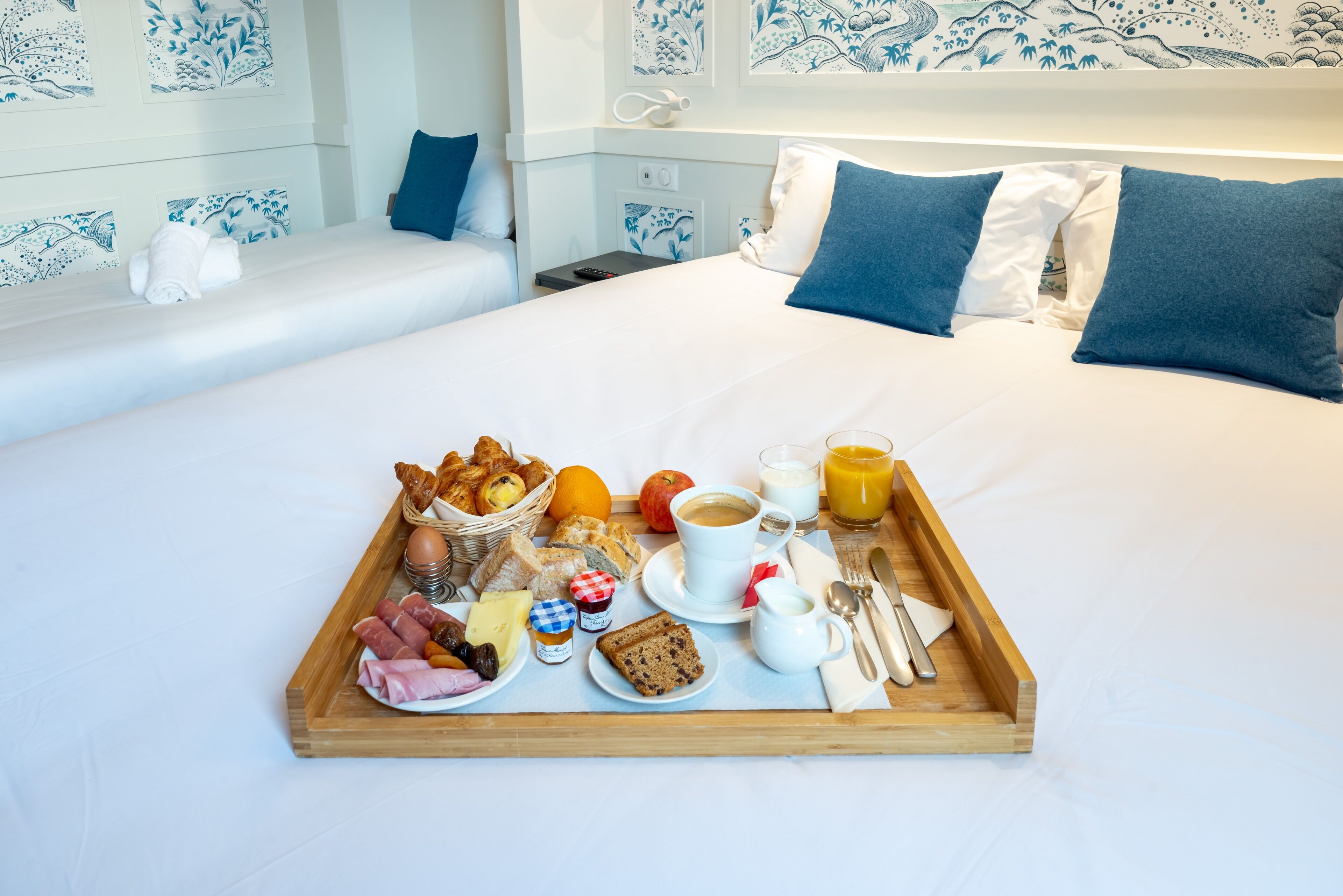Bandeja de café da manhã bem arrumada sobre a cama, com cabeceira estampada em azul e branco.