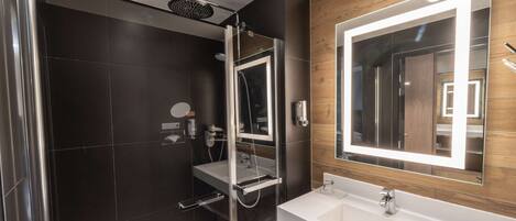 Un baño moderno con ducha envuelta en cristal, un espejo grande con iluminación integrada y un lavabo blanco.
