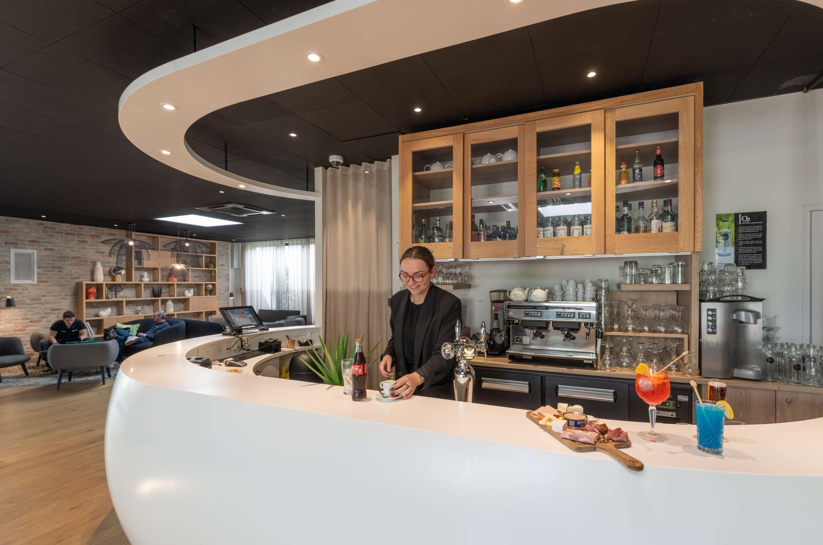 A modern bar area with a curved counter, wooden cabinets with glass doors, and a coffee machine.