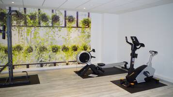 Un gimnasio con equipo de ejercicio, incluyendo una cinta de correr y una bicicleta estática, y una pared decorada con plantas colgantes.
